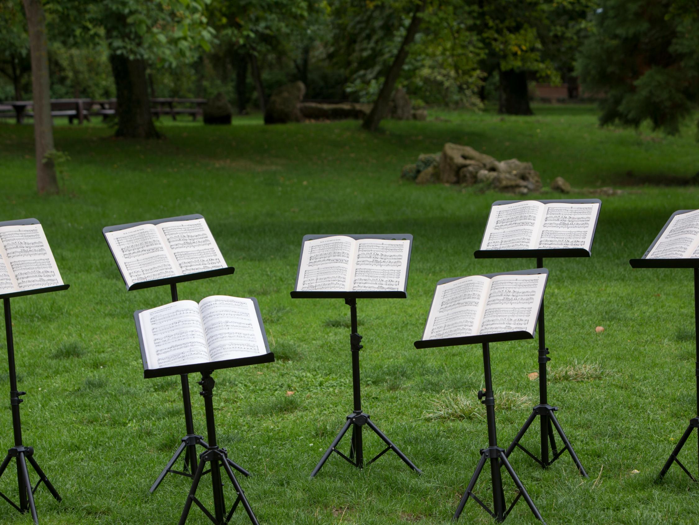 Mehrere Notenständer mit offenen Notenblättern auf einer Wiese im Park.