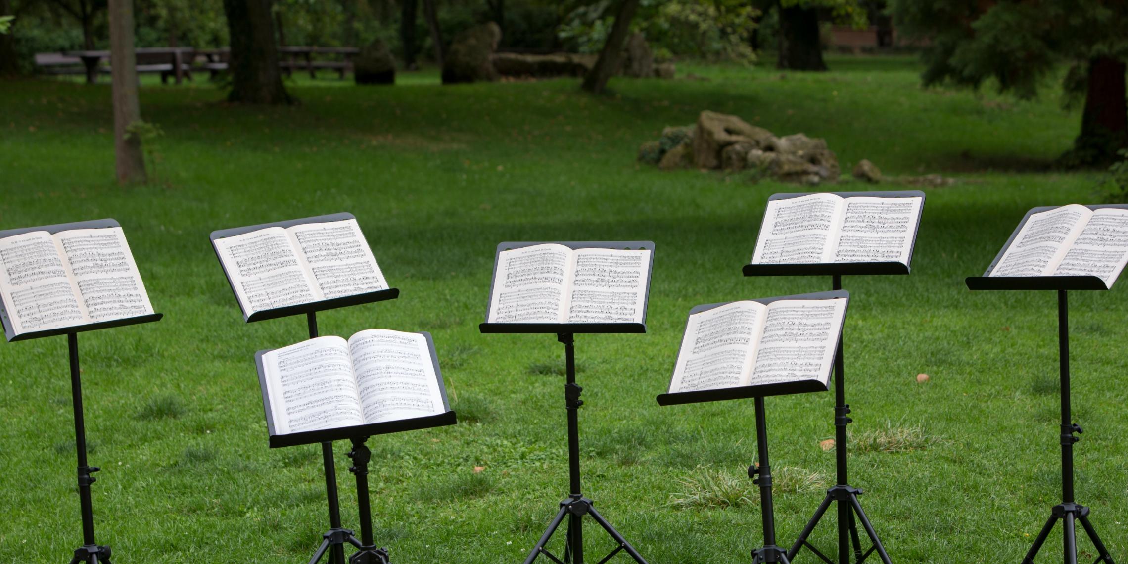 Mehrere Notenständer mit offenen Notenblättern auf einer Wiese im Park.